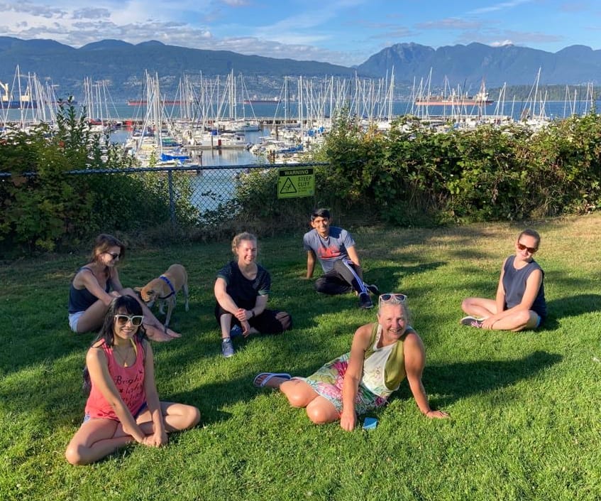 Group photo of lab team sitting in grass at a Highbury park in Vancouver with sailboats and mountains behind.